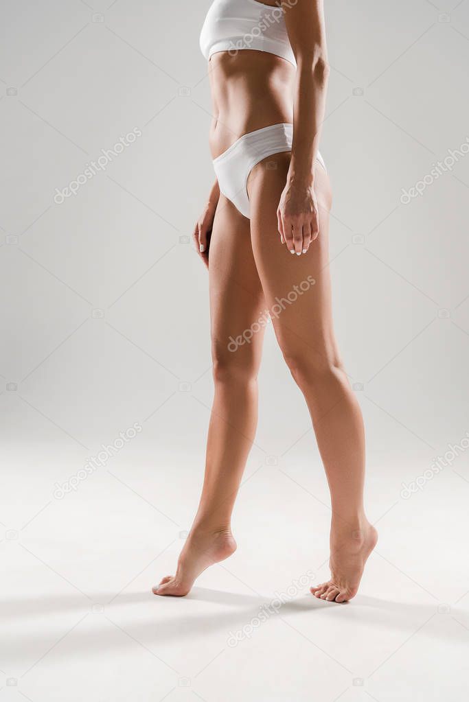 cropped view of beautiful slim woman standing on tiptoe on grey background