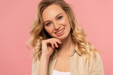 Gülümseyen sarışın kadın, elleri çenesinde, pembe tenli.