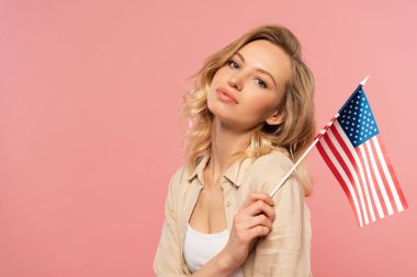 Amerikan bayrağını elinde tutan çekici kadın pembe üzerinde izole edilmiş.