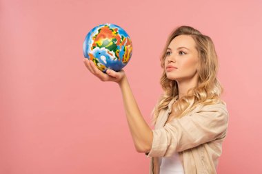Elinde dünyayı tutan sarışın kadın pembe üzerinde izole edilmiş.