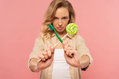 Sarışın kadın diş fırçası ve lolipop tutuyor. Pembe üzerine izole edilmiş.