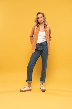 Çekici bir genç kadın sarı arka planda kameraya bakıyor.