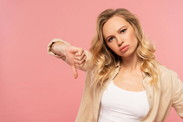 Sad woman showing thumb down gesture isolated on pink