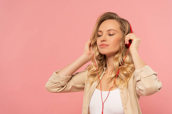 Blonde woman with closed eyes in headphone isolated on pink