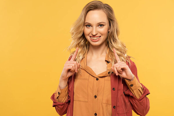 Smiling woman pointing up with fingers isolated on yellow