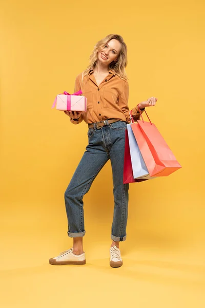 Χαμογελαστή Γυναίκα Κρατώντας Κουτί Δώρου Και Τσάντες Ψώνια Κίτρινο Φόντο — Φωτογραφία Αρχείου