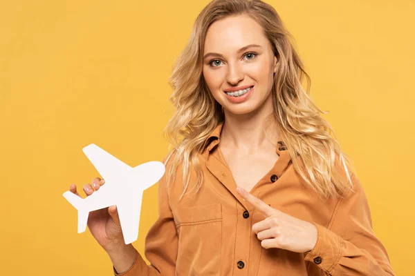 Улыбающаяся Блондинка Указывающая Бумажный Самолет Изолированный Желтый — стоковое фото