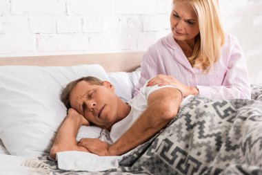 Worried woman waking up snoring husband in bed clipart