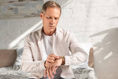 Adam yatakta otururken kol saatine bakıyor.