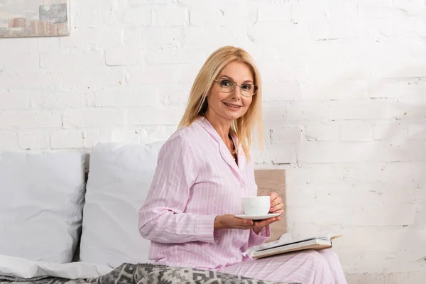 Femme Souriante Avec Café Livre Assis Sur Lit — Photo