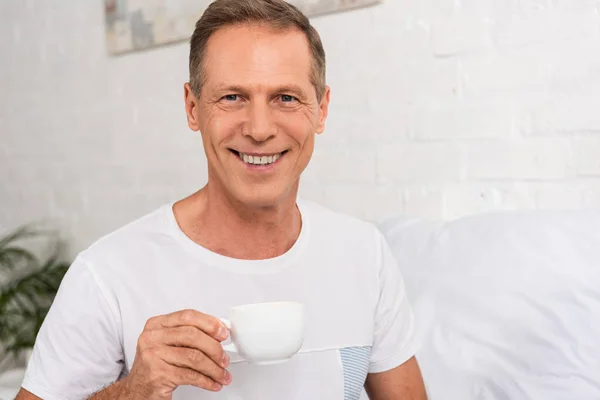 Uomo Che Tiene Tazza Caffè Sorride Alla Fotocamera Camera Letto — Foto Stock