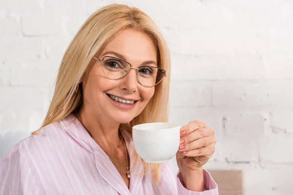 Mujer Sonriente Con Anteojos Pijamas Sosteniendo Taza Café Mirando Cámara —  Fotos de Stock