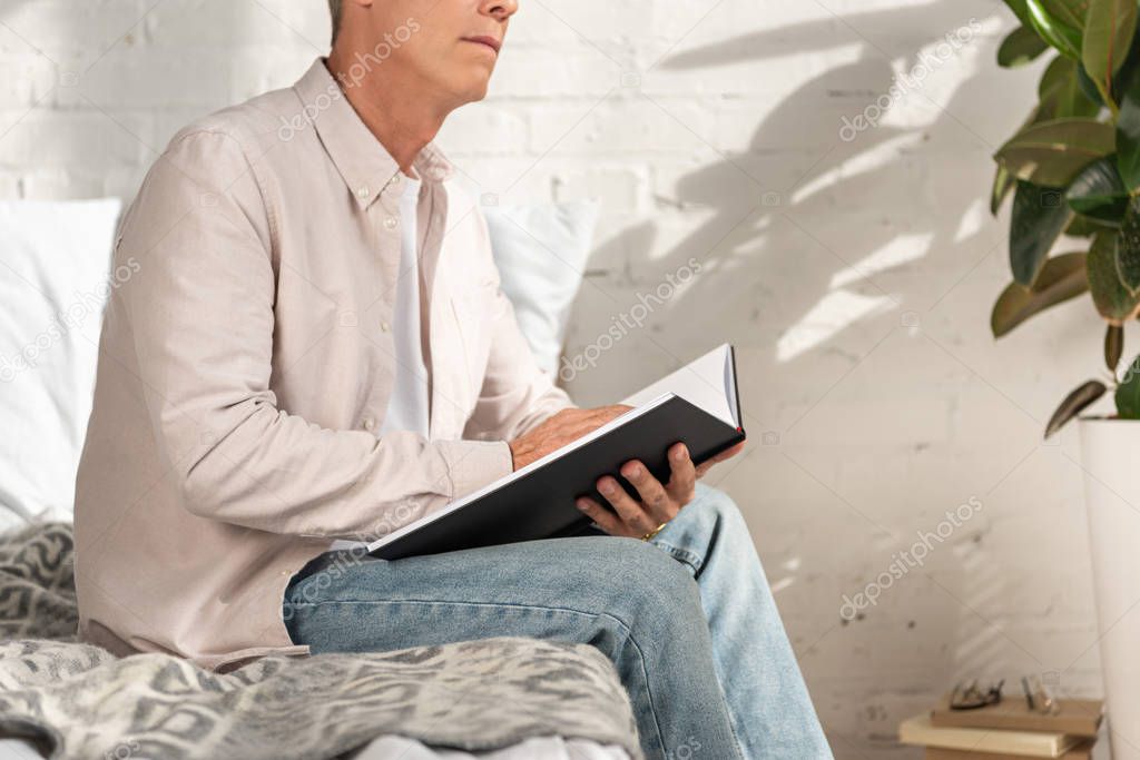Cropped view of man holding notebook on bed