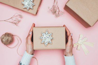 Kırpılmış bir kadının Noel hediyelerini kağıt, sicim ve çiçeklerle paketlediği pembe bir manzara.