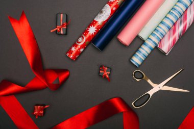top view of wrapping paper rolls, scissors and little gift boxes on black clipart