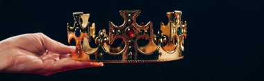 cropped view of woman holding golden crown with gemstones, isolated on black, panoramic shot clipart