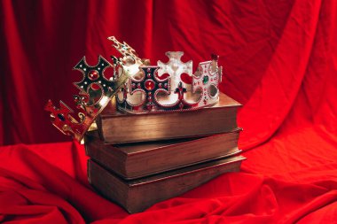 ancient golden and silver crowns with gemstones on books on red cloth clipart