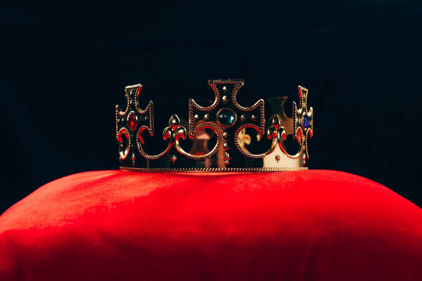 античная золотая корона с драгоценными камнями на красной подушке, изолированные на черном

