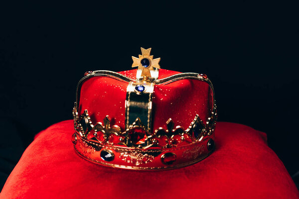 древняя золотая корона с драгоценными камнями на красной подушке, изолированные на черном
