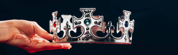 cropped view of woman holding silver crown with gemstones, isolated on black, panoramic shot