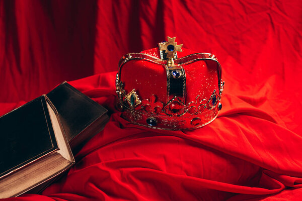 ancient golden crown with gemstones on red cloth with books