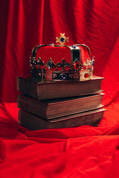 древняя золотая корона с драгоценными камнями на книгах на красной ткани
