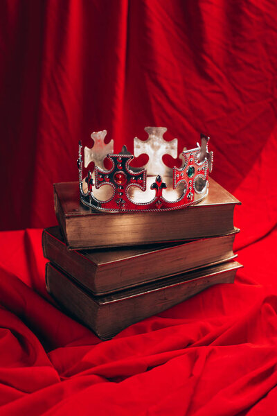 ancient silver crown with gemstones on books on red cloth