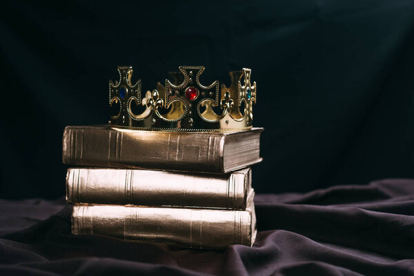 древняя золотая корона с драгоценными камнями на книгах на черной ткани
