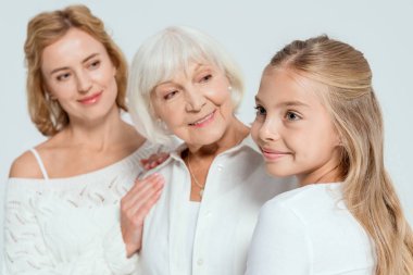 Gülümseyen torun, anne ve büyükannenin seçici odak noktası. Gri arka planda ona bakıyor. 