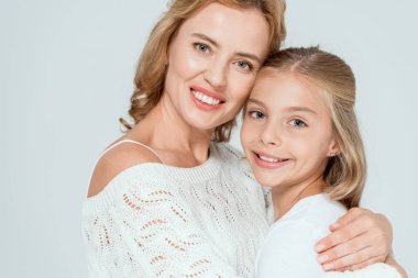 Çekici anne gülümseyen kızı kucaklıyor ve gri renkli kameraya bakıyor. 