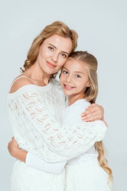 Çekici anne gülümseyen kızı kucaklıyor ve gri renkli kameraya bakıyor. 