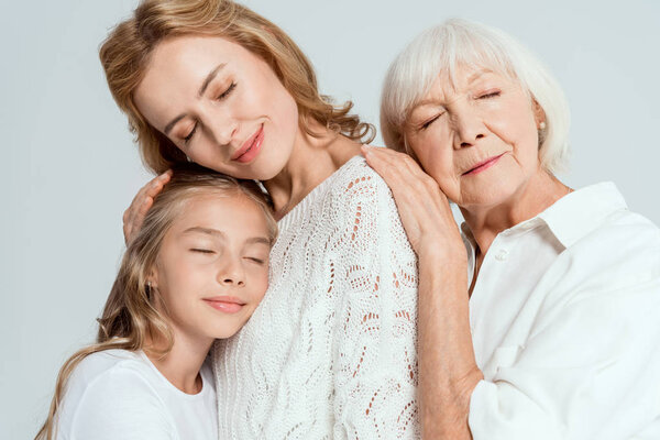 smiling granddaughter, mother and grandmother with closed eyes hugging isolated on grey 