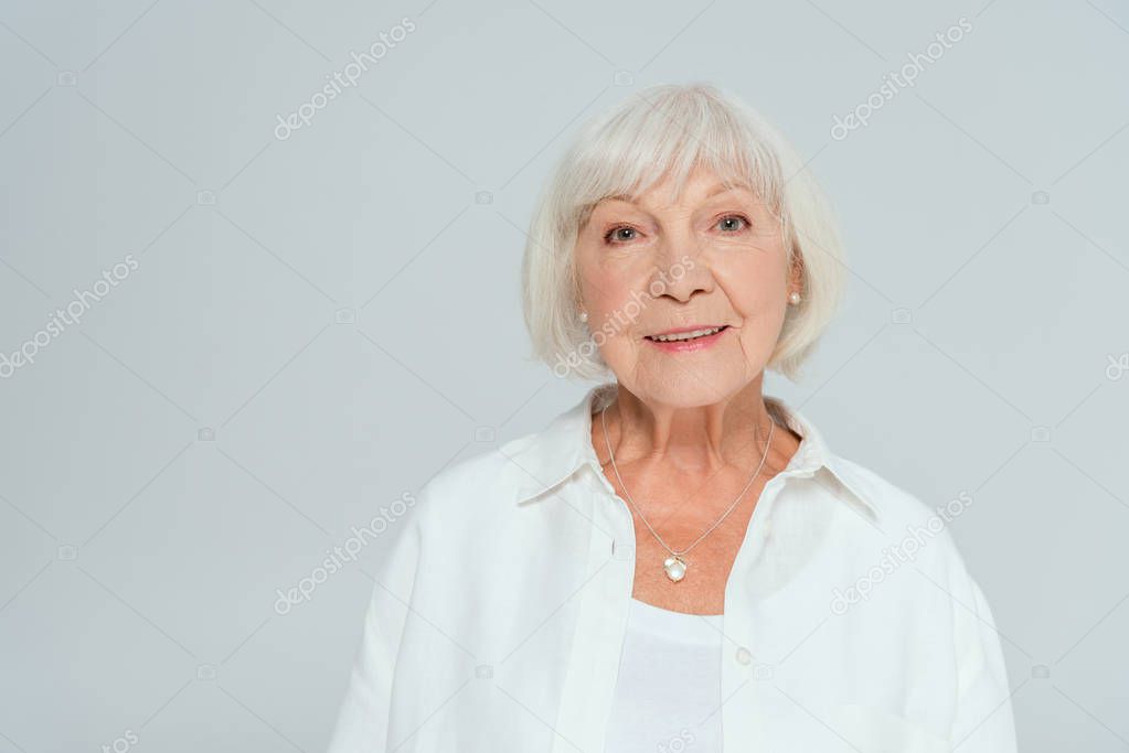 attractive and smiling woman looking at camera isolated on grey 