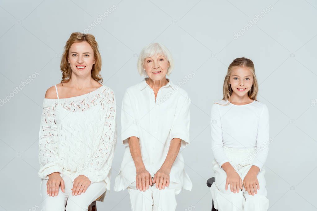 smiling granddaughter, mother and grandmother looking at camera isolated on grey 