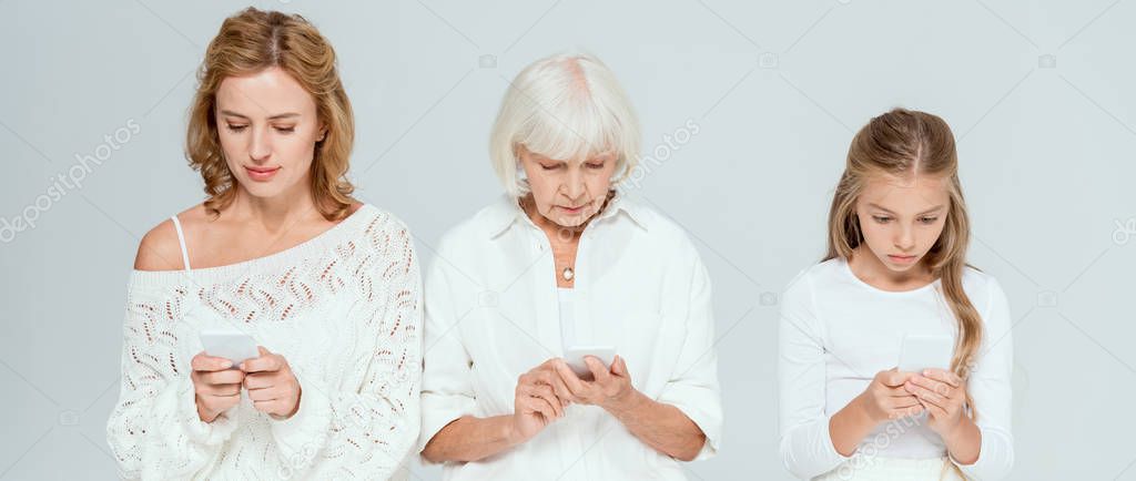 panoramic shot of granddaughter, mother and grandmother using smartphones isolated on grey 
