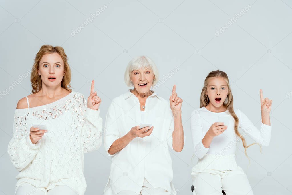 shocked granddaughter, mother and grandmother holding smartphones and showing idea gestures isolated on grey 