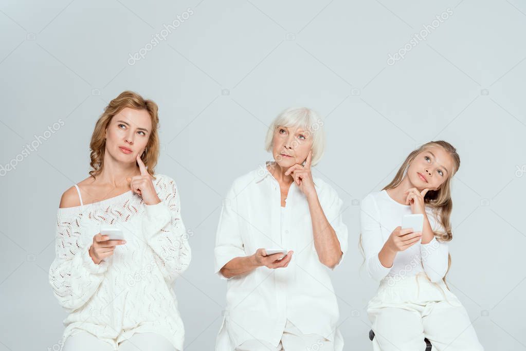 pensive granddaughter, mother and grandmother holding smartphones isolated on grey 