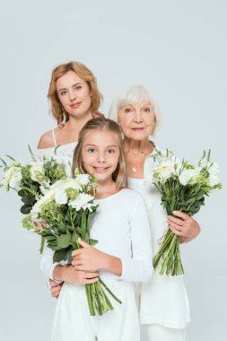 Gülümseyen torun, anne ve büyükanne gri renkte buketler tutuyorlar. 