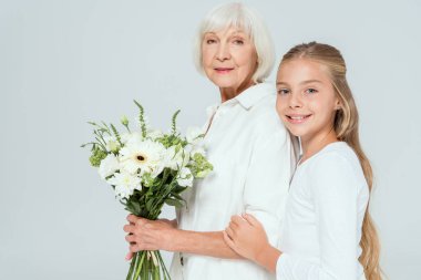 Gülümseyen torun. Gri renkte bir buketle büyükanneye sarılıyor. 