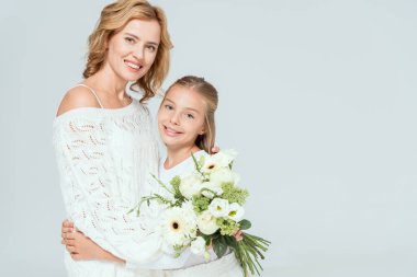 Gülümseyen kız, gri renkte bir buketle çekici anneye sarılıyor. 