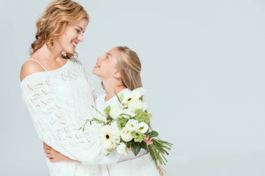 Gülümseyen kız, gri renkte bir buketle çekici anneye sarılıyor. 