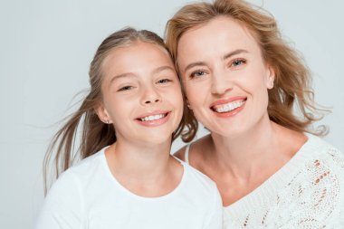 attractive and smiling mother and daughter looking at camera isolated on grey  clipart