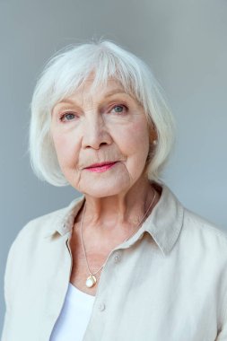 Gri gömlekli çekici kadın kameraya bakıyor.