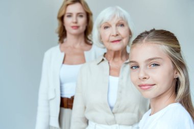 selective focus of smiling granddaughter and grandmother, mother on background isolated on grey  clipart