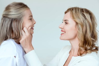 Çekici anne, gri üzerine izole edilmiş gülümseyen kızının yanaklarına dokunuyor. 