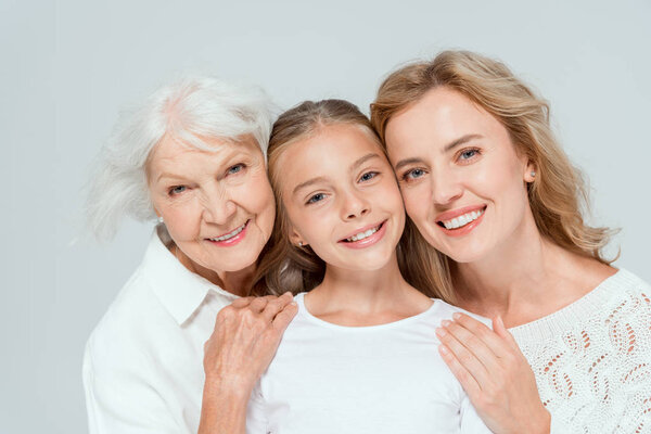 smiling mother and grandmother hugging granddaughter isolated on grey 