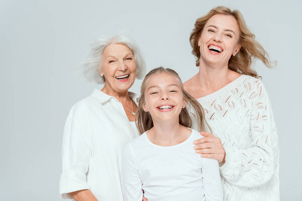 smiling granddaughter, mother and grandmother looking at camera isolated on grey 