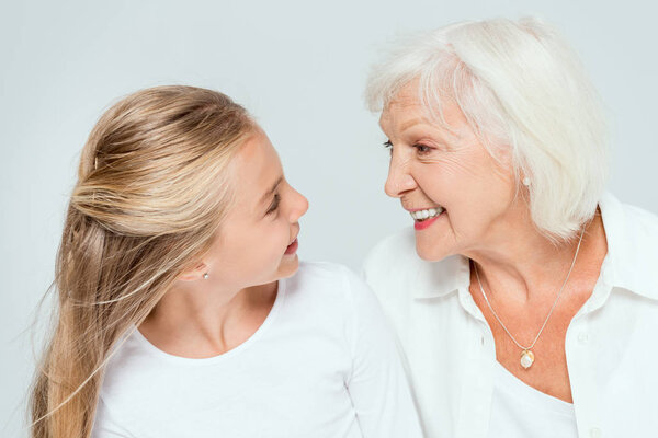 улыбающиеся внучка и бабушка смотрят друг на друга, изолированные от серых
 