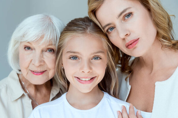 mother, grandmother and smiling granddaughter looking at camera isolated on grey 