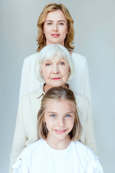 smiling granddaughter, grandmother and mother looking at camera isolated on grey 
